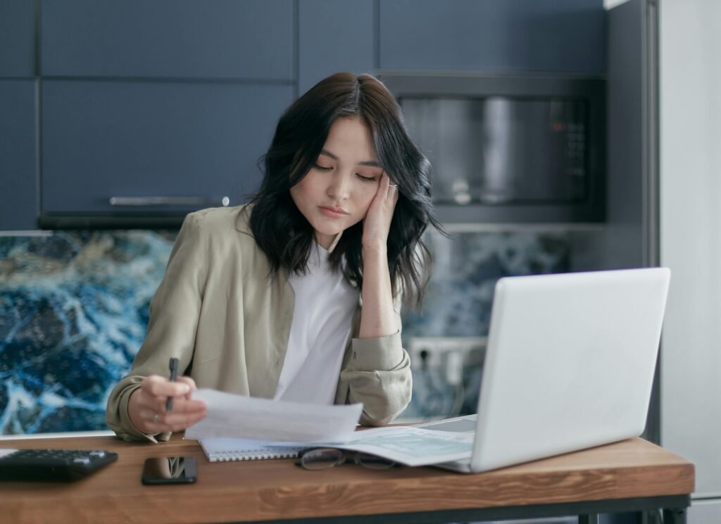 Young woman working from home, analyzing documents with laptop and smartphone on a desk.